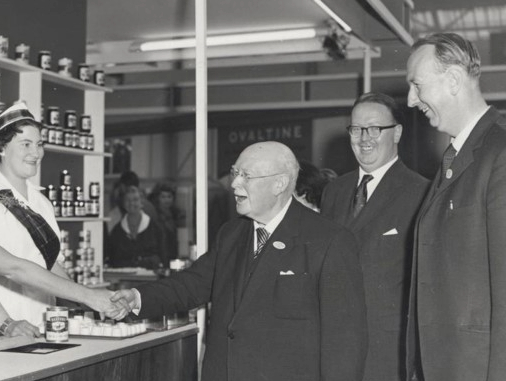 A black and white images shows William Baxter visiting a trade stand, where soups from Baxters of Speyside are being showcased. Behind William are his sons Gordon and Ian. 